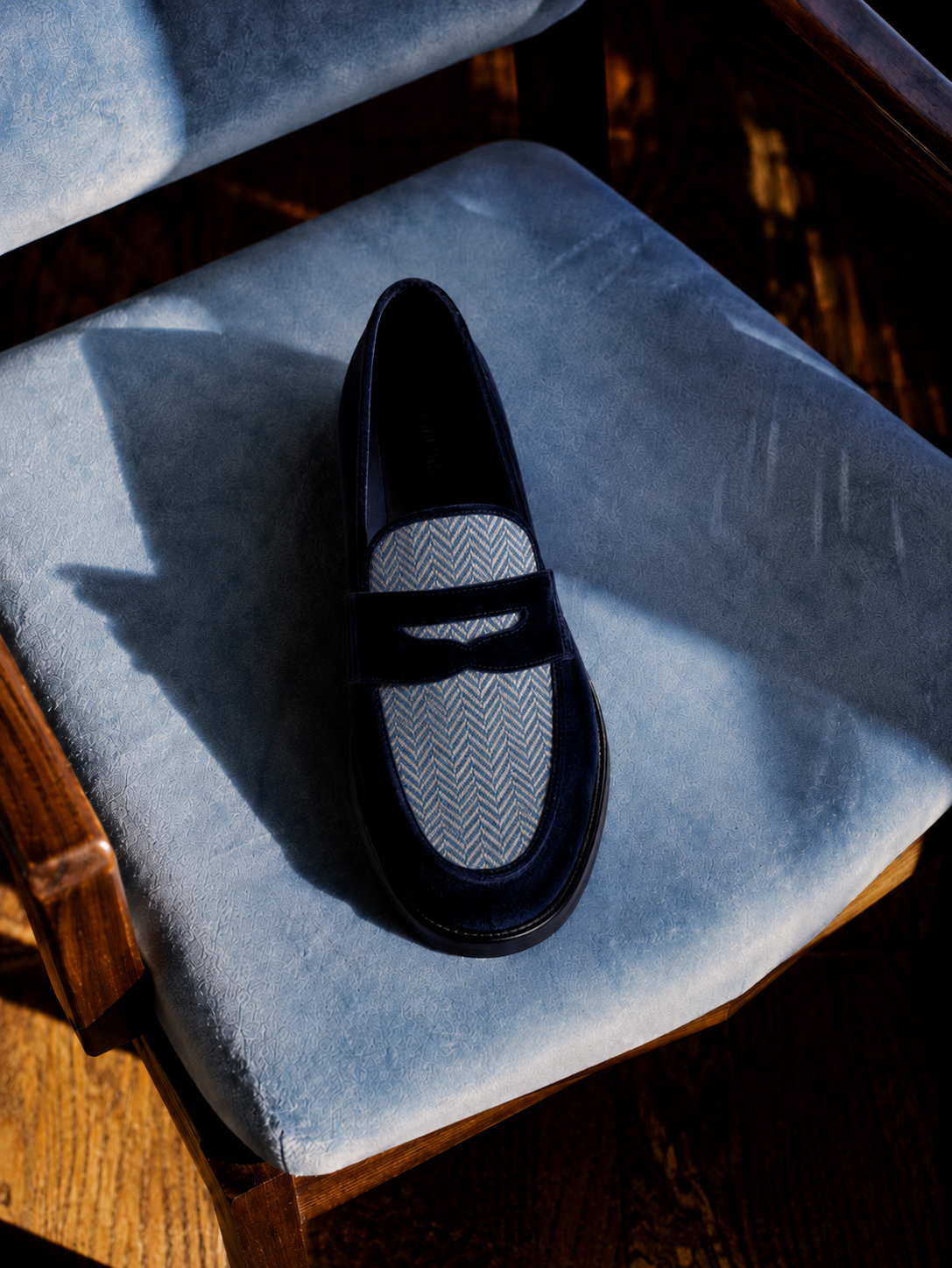 Navy velvet LYL penny loafer with a blue herringbone insert on a pale blue chair